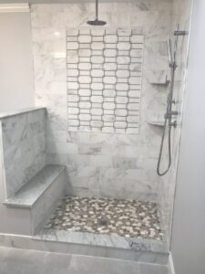 A beautifully tiled shower with a pebble floor and decorative accent tile by Prenga Remodeling in Orange, CT