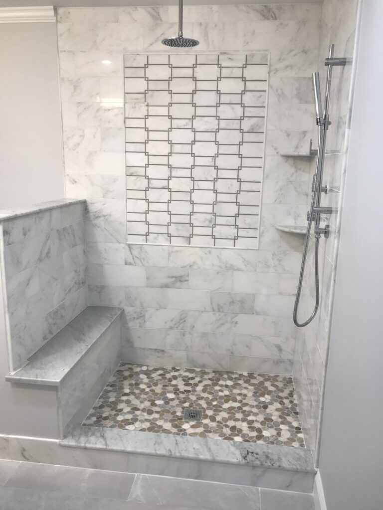 A beautifully tiled shower with a pebble floor and decorative accent tile by Prenga Remodeling in Orange, CT