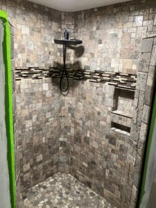 A newly tiled shower with a unique pebble floor, part of a bathroom remodel by DCM Multi Service llc in Harrisburg, PA.