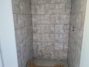 Newly tiled shower stall with grey wall and white hexagonal floor tiles by K. MCGHEE CONSTRUCTION LLC in Montgomery, AL.