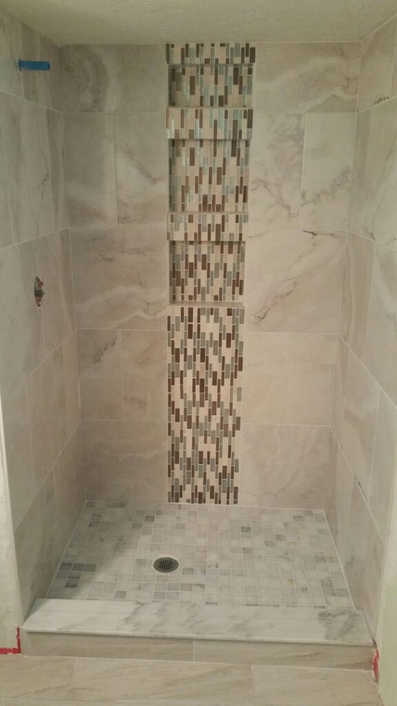 A newly tiled shower stall featuring a decorative vertical mosaic tile strip by ALKA Construction/ Handyman Services in Layton, UT