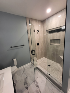 A modern tiled shower with a glass enclosure and toilet in a renovated bathroom by Nance Brothers, LLC in Matthews, NC.