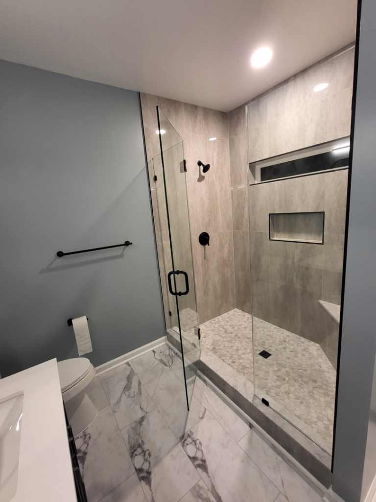A modern tiled shower with a glass enclosure and toilet in a renovated bathroom by Nance Brothers, LLC in Matthews, NC.