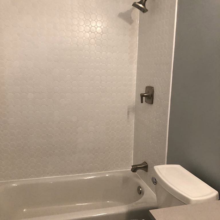 A bathroom with a newly tiled shower and tub combination featuring small hexagonal tiles by Ruach Home Services in Laurel, MD.