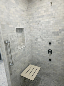 A beautifully tiled shower with a grab bar and fold-down seat installed by Tyler the Tiler in Jefferson, WI.