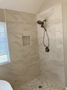 A newly tiled walk-in shower featuring a built-in niche and modern shower fixtures by J.C.Improvement in Katy, TX.