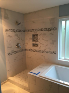 A tiled shower with decorative mosaic strips and built-in niches in a bathroom remodel by Bailey Contracting, LLC in Lake Oswego, OR.