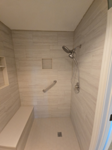 A custom tiled walk-in shower with a built-in bench and safety grab bar by The Shower Company in Kansas City, MO.
