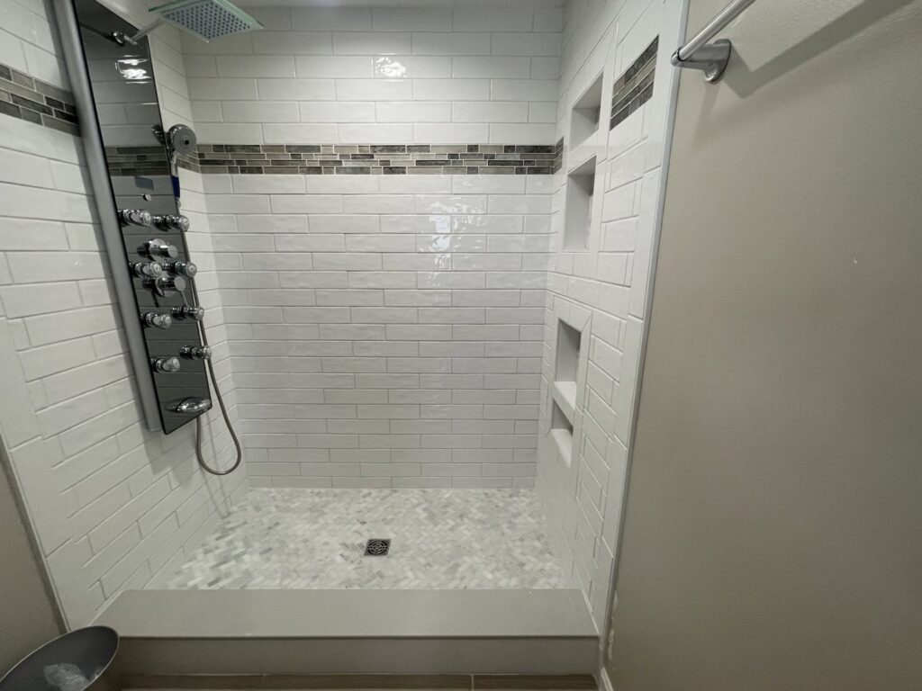 A newly installed walk-in shower with white subway tiles, built-in niches, and modern fixtures by Inspired Renovation & Hardscape's in Lorain, OH.