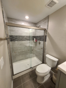 A newly installed walk-in shower with grey and mosaic tiles in a bathroom by QCON LLC in Aurora, CO.