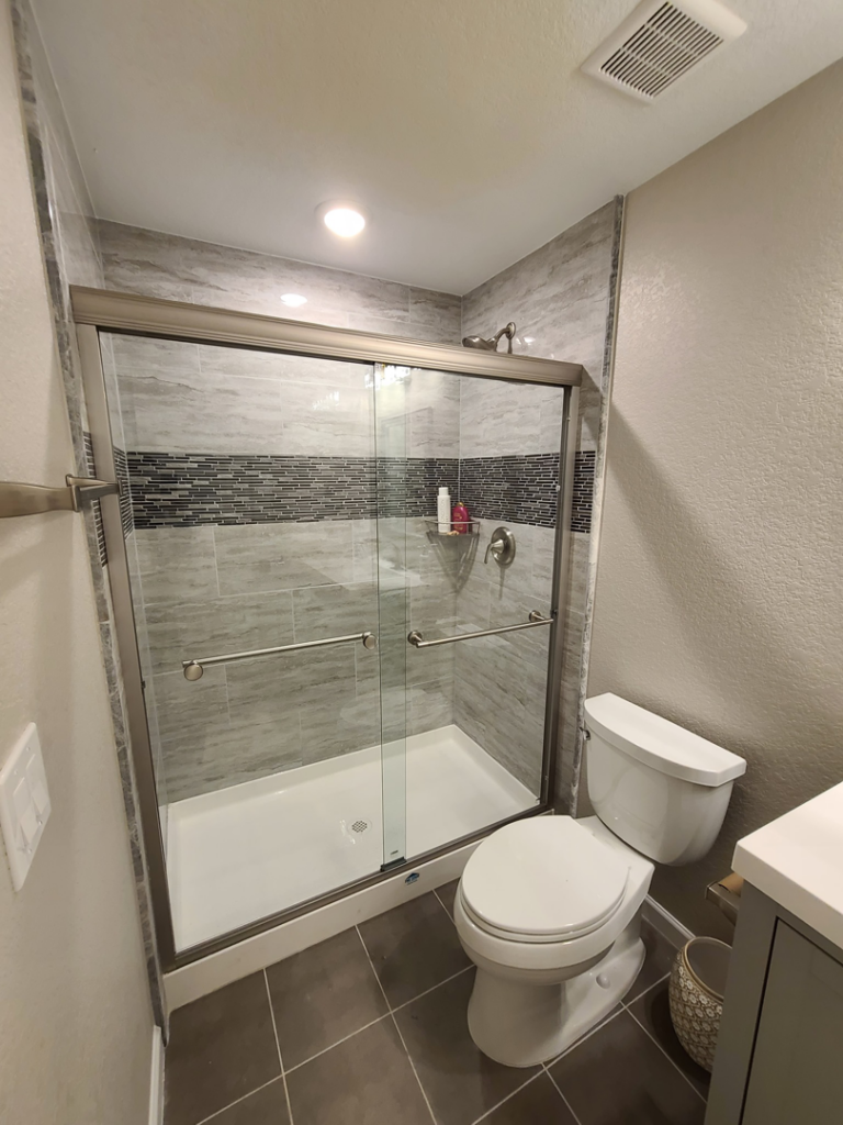 A newly installed walk-in shower with grey and mosaic tiles in a bathroom by QCON LLC in Aurora, CO.