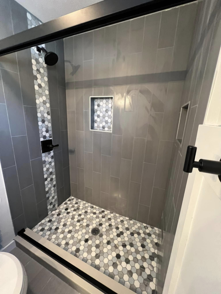 A newly tiled walk-in shower with grey and white hexagonal floor tiles installed by Roempagel Renovations LLC in South Bend, IN.