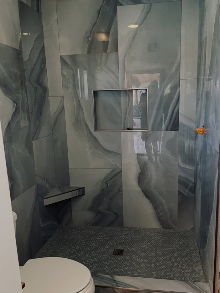 A beautifully tiled walk-in shower with a built-in niche and corner shelf, expertly installed by AGM Remodeling LLC in Scottsdale, AZ.