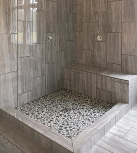A beautifully tiled walk-in shower with a pebble floor and built-in bench by Clean Cut Tile LLC in St. Louis, MO.