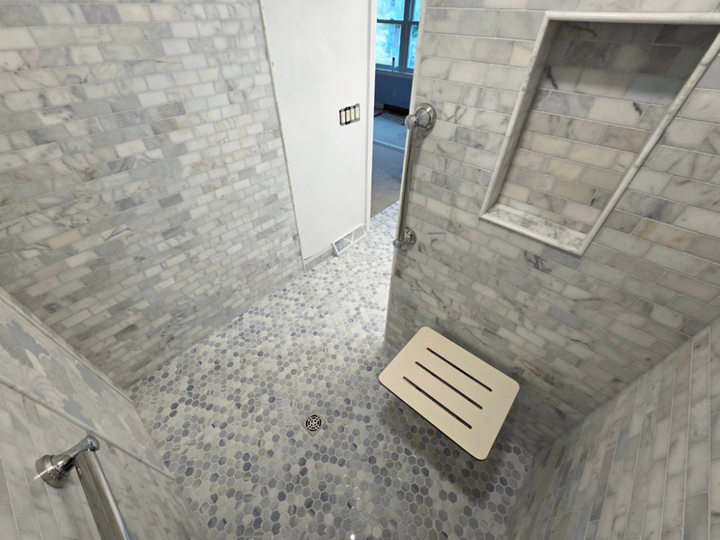 A newly tiled walk-in shower with a built-in niche and fold-down seat by Tyler the Tiler in Jefferson, WI.