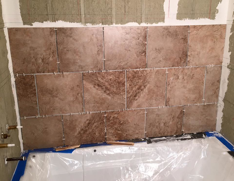Brown tiles being installed on a bathroom shower wall with spacers, showing a tiling job in progress by I'll Fix It in Shawnee, KS.