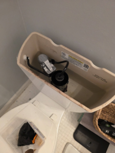 A toilet tank with the flushing mechanism visible, indicating a plumbing repair by Turner Family Services LLC in Columbus, GA.