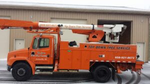 An orange bucket truck with Top Down Tree Service LLC branding parked in Janesville, WI during winter