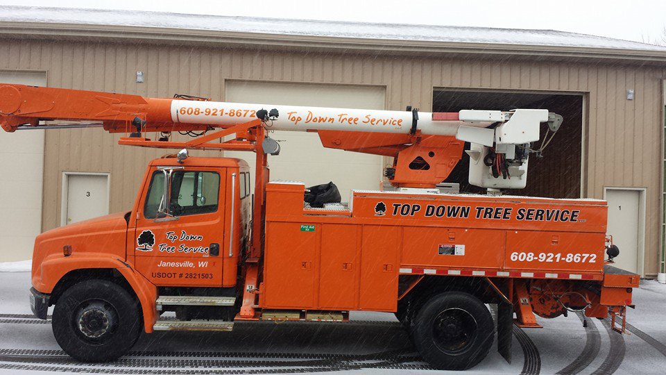 An orange bucket truck with Top Down Tree Service LLC branding parked in Janesville, WI during winter