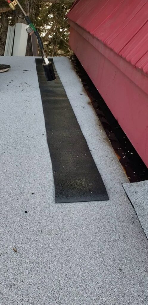 A worker applying torch-down roofing material on a flat roof, a service offered by Jesse Roofs Co. in Denver, CO