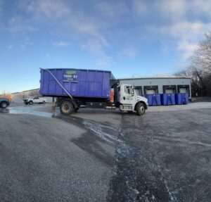 A Toss-It truck with a blue dumpster at a commercial loading dock, with multiple dumpsters ready for service in Baltimore, MD.