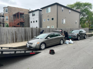 A tow truck preparing a grey sedan for junk car removal on a residential street for A+ Towing Cash for Junk Cars in Melrose Park, IL.
