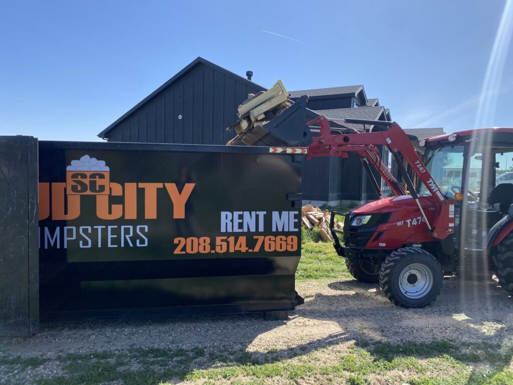 A tractor loading construction debris into a SpudCity Dumpsters roll-off bin in Caldwell, ID.