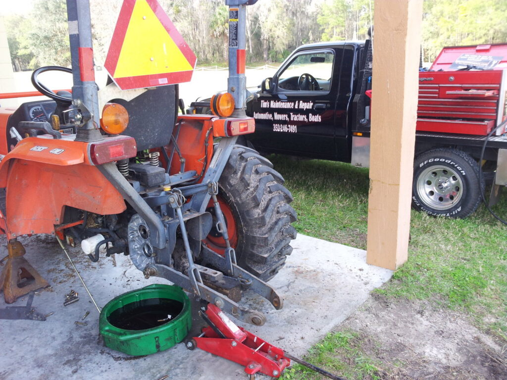 A tractor undergoing maintenance with an oil pan and jack, serviced by Tim's Maintenance & Repair in Las Vegas, NV