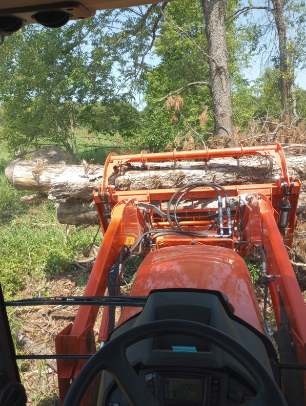 A tractor moving a large log with a front loader for land clearing by Todd's Mini-Tractor/Backhoe Services in Appleton, WI.