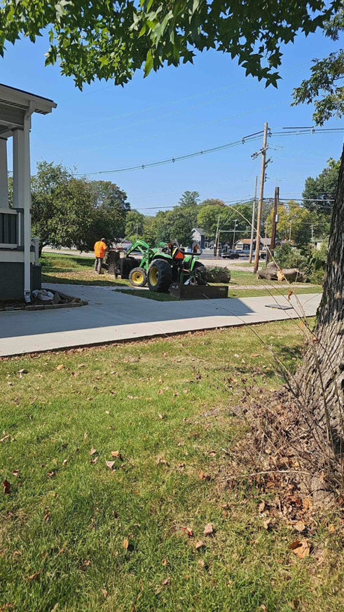 A tractor with a front loader removing cut tree branches and debris from a residential property for Mike's tree service in St. Louis, MO.