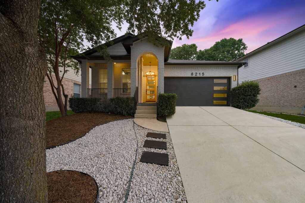 A beautifully updated traditional home exterior with modern garage door and landscaping by HomeNovate in San Antonio, TX.