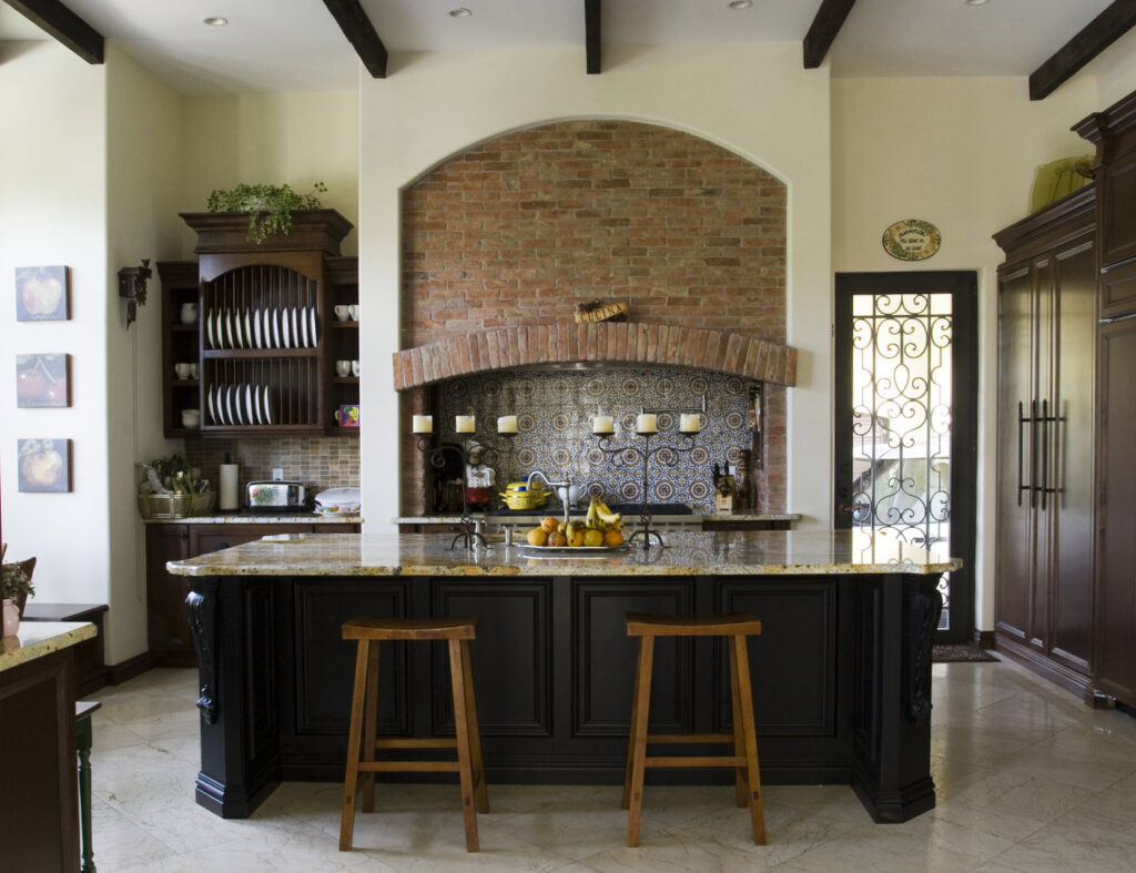 A traditional kitchen featuring a large dark island and a rustic brick accent wall by Madison Construction Group, Inc. in Miami, FL