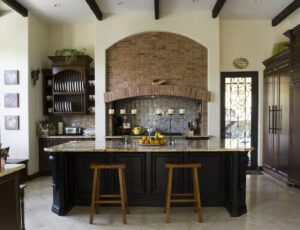A traditional kitchen featuring a large dark island and a rustic brick accent wall by Madison Construction Group, Inc. in Miami, FL