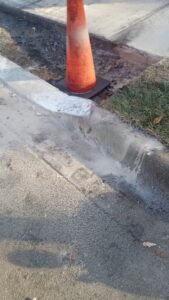An orange traffic cone next to a newly finished concrete curb, showing general contractor work by National Kurb Kut in Naperville, IL.