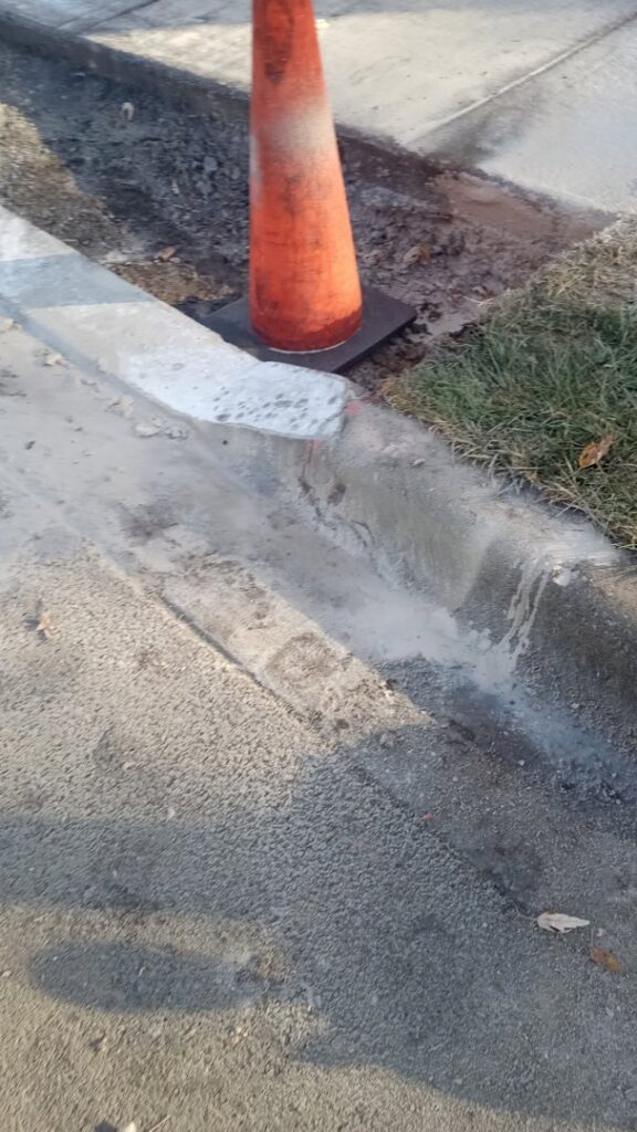 An orange traffic cone next to a newly finished concrete curb, showing general contractor work by National Kurb Kut in Naperville, IL.