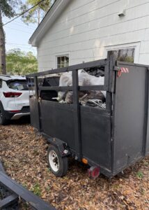 A black utility trailer filled with trash bags and debris, ready for junk removal by Reliable Pro in Tallahassee, FL.