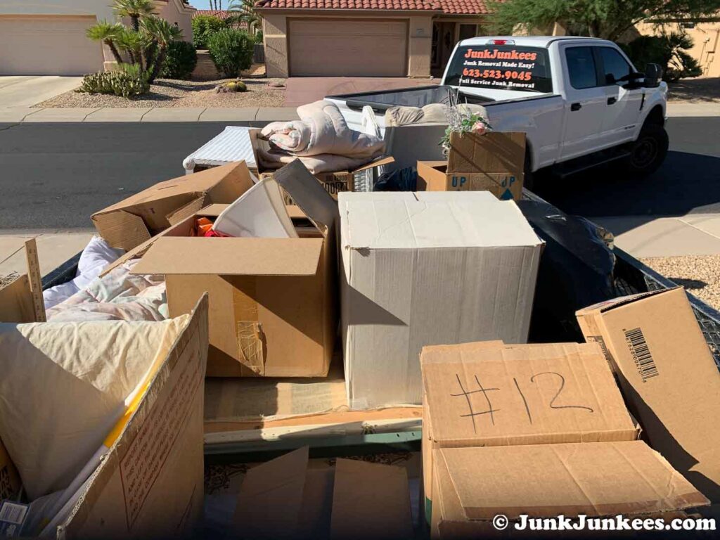 A Junk Junkees truck and trailer loaded with cardboard boxes and various items for removal in Peoria, AZ.