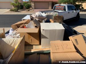 A Junk Junkees truck and trailer loaded with cardboard boxes and various items for removal in Peoria, AZ.