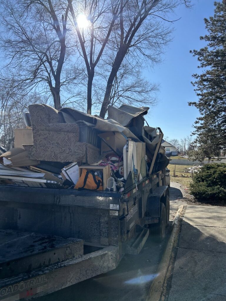A trailer loaded with household junk and debris under a bright sky for removal by The Goat Junk Removal in Ankeny, IA
