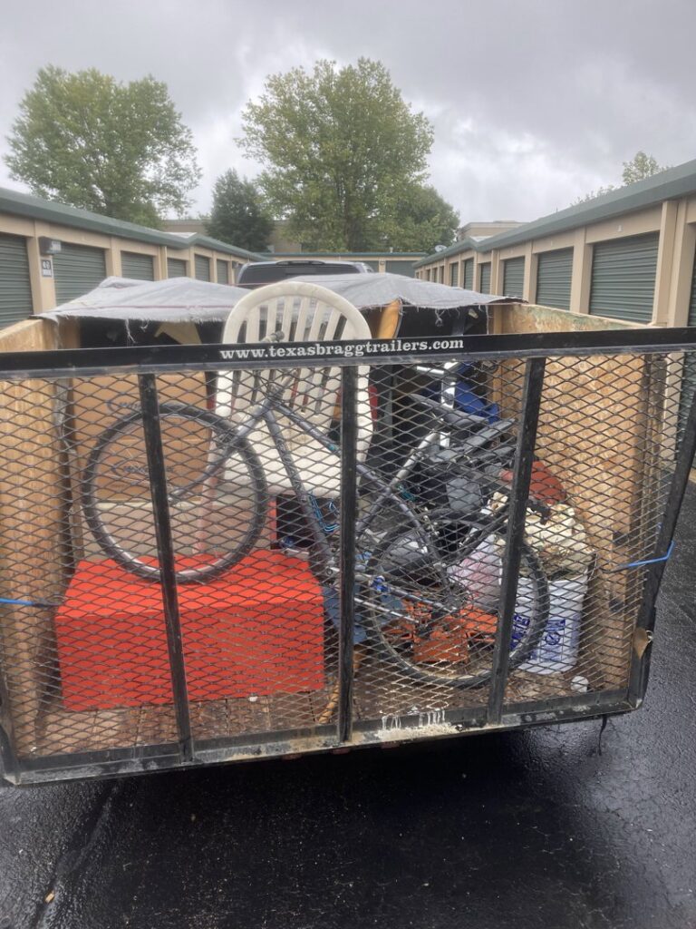 A trailer full of various junk items like a bicycle and chairs in front of storage units for Trash It All Hauling And Junk Removal LLC in Fort Collins, CO.