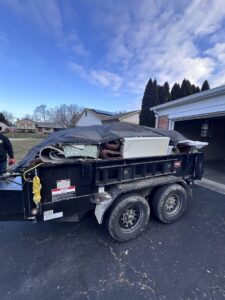 A trailer fully loaded with old carpets, an appliance, and other debris, covered by a tarp for 614junkremoval in Columbus, OH.