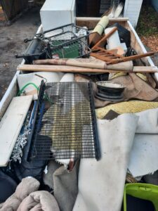 A trailer loaded with various junk items such as carpets, furniture, and a metal grate, for removal by Sunshine junk removal LLC in Lake City, MN.