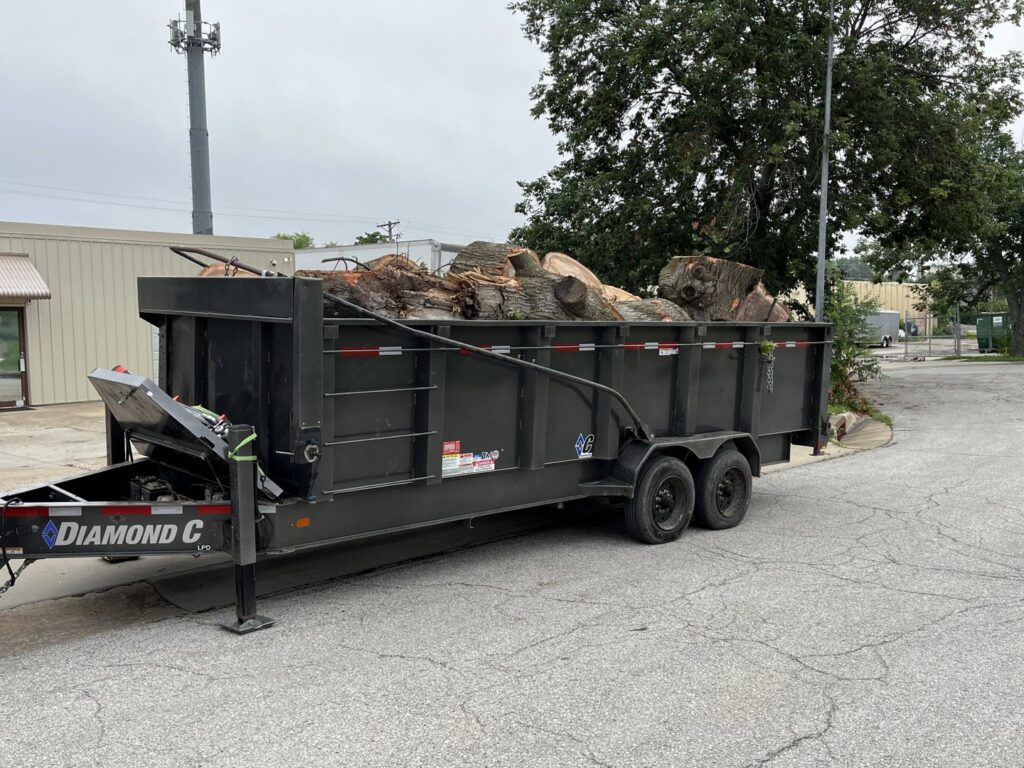 A heavy-duty trailer filled with cut logs and wood debris from a tree removal project by Happy Lemon Tree Service in Belton, MO.