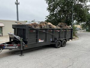 A heavy-duty trailer filled with cut logs and wood debris from a tree removal project by Happy Lemon Tree Service in Belton, MO.