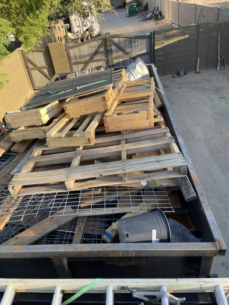 A trailer filled with wooden pallets, metal grates, and various debris for removal by Canyon State Junk Removal in Peoria, AZ
