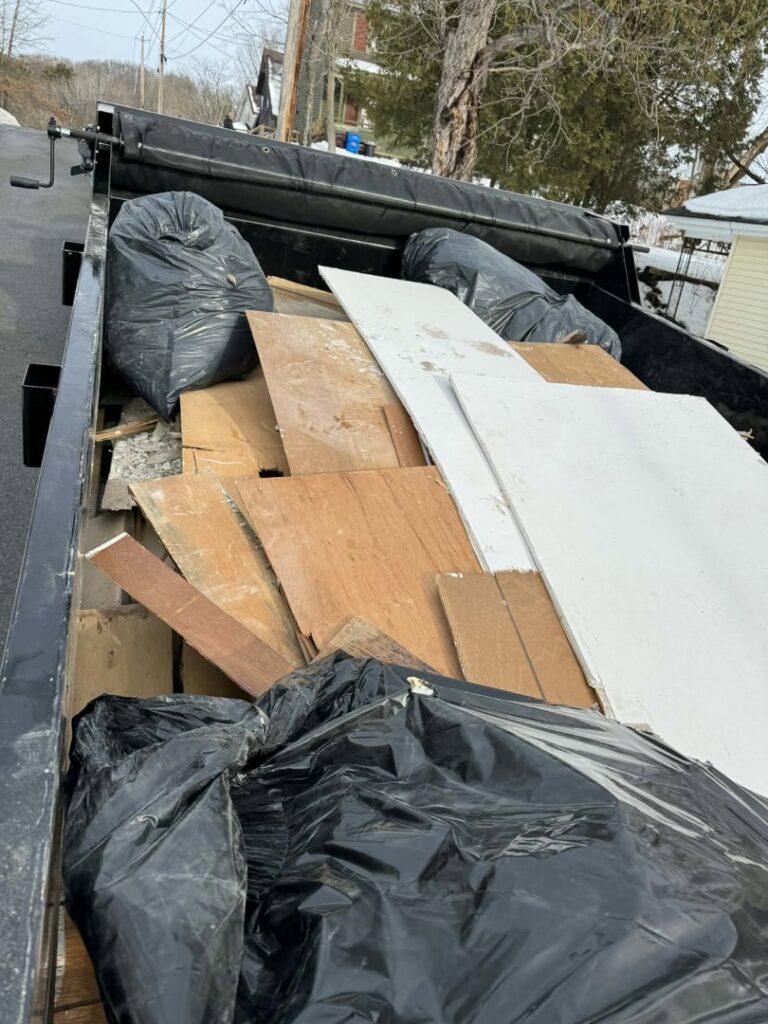 A junk removal trailer loaded with wood planks, black trash bags, and construction debris by Clutter Bandit in Albany, NY.