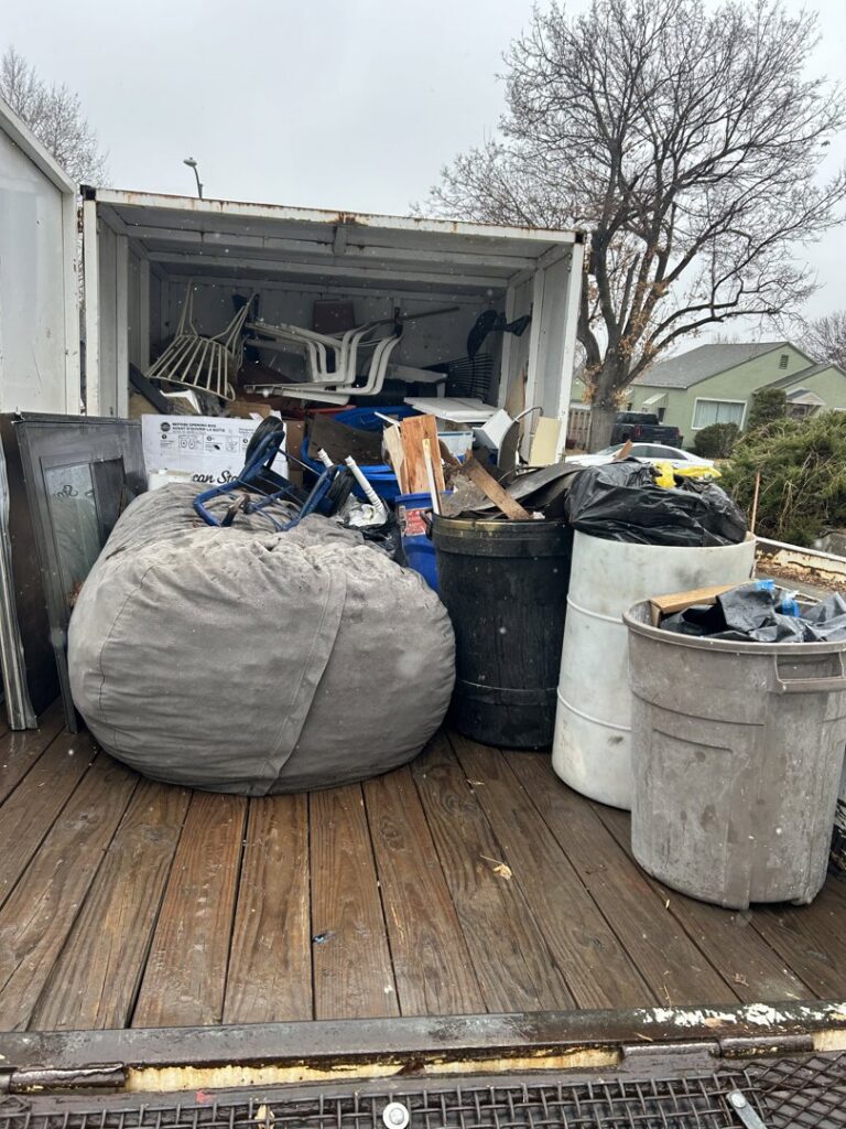 A trailer loaded with a large bean bag chair, trash cans, and various chairs, demonstrating a junk removal service by Empty It Out Junk Removal, LLC in Billings, MT.