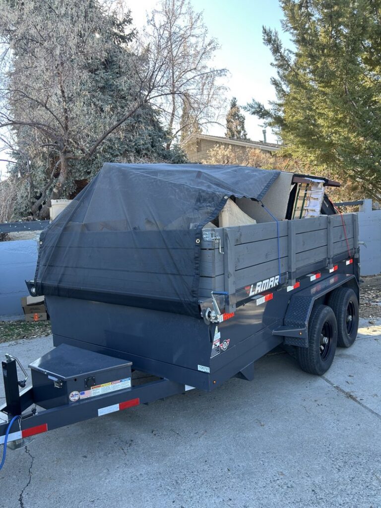 A junk removal trailer loaded with furniture and boxes, covered with a tarp, parked in a driveway by Reno Junk Pros in Reno, NV.