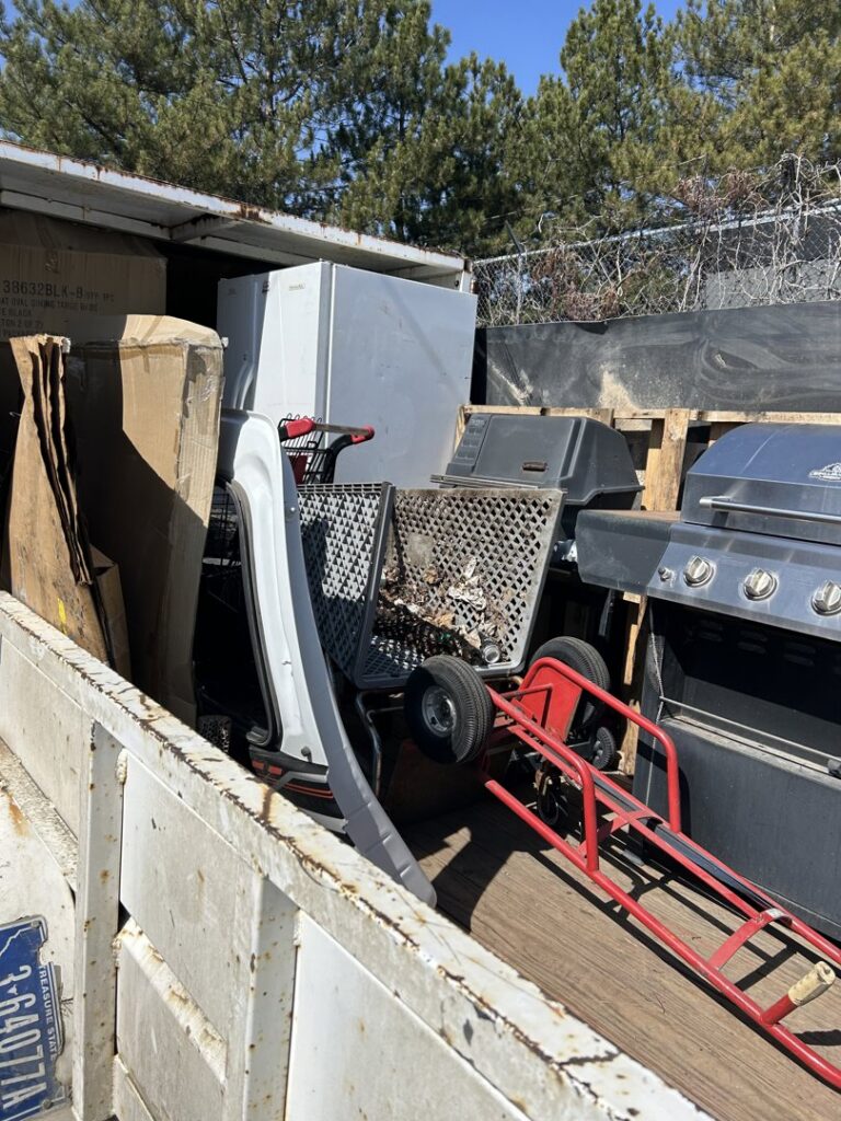 A trailer loaded with a refrigerator, grill, and shopping carts, showcasing a large item junk removal service by Empty It Out Junk Removal, LLC in Billings, MT.