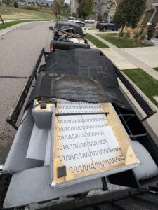 A trailer loaded with various furniture items, including sofa frames and cushions, covered with a net for transport by Goblins Junk Removal in Wheat Ridge, CO.